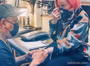 Фото: мастер тату в маске и клиент во время сеанса татуировки, демонстрирующее процесс нанесения рисунка крупным планом.