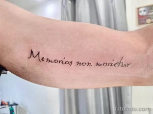 Фото тату с латинской фразой 'Memórias non moriuntur' на предплечье. Изящный шрифт, минималистичный дизайн, черные чернила на светлой коже.