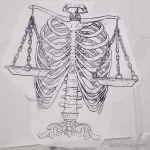 Необычный эскиз татуировки Весы в виде скелета, держащего весы. Выполнен в черно-белой графике с детализированной прорисовкой костей.