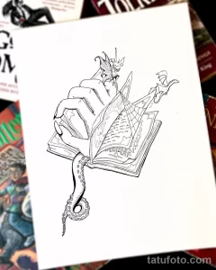 Черно-белое фото тату с изображением дракона, читающего раскрытую книгу. Детализированный рисунок с элементами готики и фэнтези.