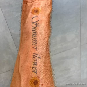 Фото тату на предплечье: надпись 'Summer flower' в окружении стилизованных желтых подсолнухов, выполненная в ярких и сочных цветах.