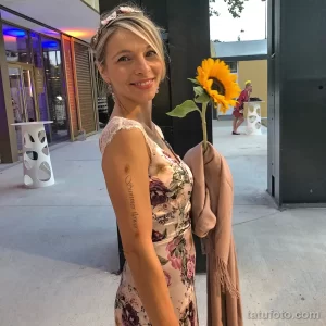 Фото тату на предплечье женщины: изящная надпись 'Summer flower' в окружении небольших желтых цветов, выполненная в нежных тонах.