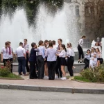 Фото тату на руке: небольшая татуировка возле фонтана, изображение цветка и абстрактных линий, выполненное в ярких цветах. Уличная фотография татуировки.
