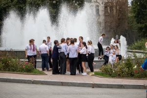 Фото тату на руке: небольшая татуировка возле фонтана, изображение цветка и абстрактных линий, выполненное в ярких цветах. Уличная фотография татуировки.