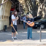 Фото тату: уличный музыкант играет на гитаре, на руке видна татуировка. Атмосферный кадр, демонстрирующий татуировку в повседневной жизни.