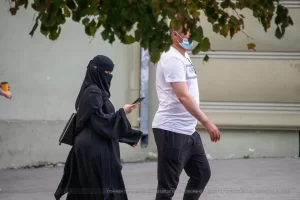 Фотография уличной моды в Одессе: женщина в черном хиджабе и мужчина в белой футболке идут по улице, женщина разговаривает по телефону.