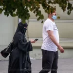 Фотография уличной моды в Одессе: женщина в черном хиджабе и мужчина в белой футболке идут по улице, женщина разговаривает по телефону.