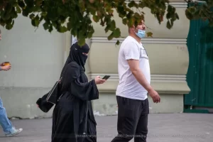 Фотография уличной моды в Одессе: женщина в черном хиджабе и мужчина в белой футболке идут по улице, женщина разговаривает по телефону.