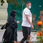 Фотография уличной моды в Одессе: женщина в черном хиджабе и мужчина в белой футболке идут по улице, разговаривая по телефону.