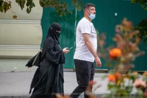 Фотография уличной моды в Одессе: женщина в черном хиджабе и мужчина в белой футболке идут по улице, разговаривая по телефону.