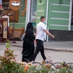 Фотография уличной моды в Одессе: женщина в черном хиджабе и мужчина в белой футболке идут по улице, держась за руки.