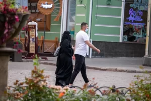 Фотография уличной моды в Одессе: женщина в черном хиджабе и мужчина в белой футболке идут по улице, держась за руки.