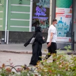 Фотография уличной моды в Одессе: женщина в черном хиджабе и мужчина в белой футболке идут по улице, демонстрируя современный стиль.
