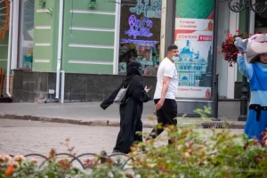 Фотография уличной моды в Одессе: женщина в черном хиджабе и мужчина в белой футболке идут по улице, демонстрируя современный стиль.