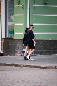 Фото тату на ноге мужчины, идущего по улице. Рисунок выполнен в стиле стрит-арт, с использованием черных линий и небольших цветовых акцентов. Мужчина одет в черную одежду.