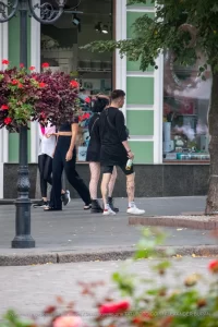 Фото тату на ноге девушки, идущей по улице. Рисунок выполнен в стиле стрит-арт, с использованием черных линий и небольших цветовых акцентов. Девушка одета в черную одежду.