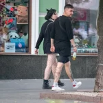 Фото тату на ноге девушки, идущей по улице. Рисунок выполнен в стиле стрит-арт, с использованием черных линий и небольших цветовых акцентов.