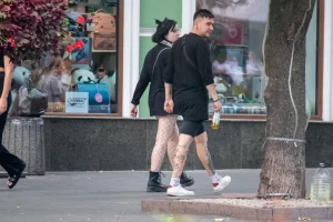 Фото тату на ноге девушки, идущей по улице. Рисунок выполнен в стиле стрит-арт, с использованием черных линий и небольших цветовых акцентов.