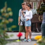 Фотография пары, где у девушки есть татуировка на ноге. Они стоят на улице, рассматривая что-то на телефоне.