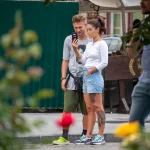 Фотография пары, где у девушки есть татуировка на ноге. Они стоят на улице, рассматривая что-то на телефоне.