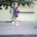 Фото тату на ноге девушки, идущей по улице. Рисунок татуировки выполнен в ярких цветах и представляет собой абстрактный узор.