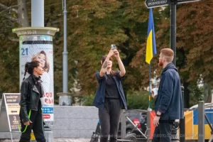 Фотография девушки с татуировкой на руке, стоящей рядом с уличным художником и рекламным щитом.