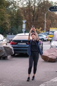 Фотография татуировки на руке девушки, делающей селфи на фоне городского пейзажа. Видны автомобили и пешеходы.