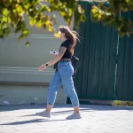 Фотография девушки с татуировкой на руке, идущей по улице. Рисунок татуировки выполнен в черном цвете и представляет собой сложный узор.