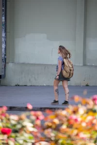 Фото тату на щиколотке девушки, идущей по улице. Рисунок татуировки выполнен в черном цвете и представляет собой растительный орнамент.