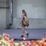 Фотография уличной татуировки: девушка идет по улице, демонстрируя татуировку на своей ноге в летней одежде.
