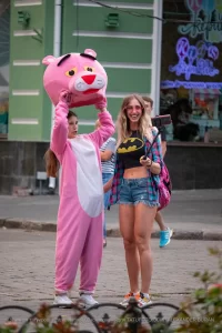 Фотография девушки в костюме розовой пантеры на улице. Девушка в розовом костюме и с головой в виде розовой пантеры, позирует на фоне городской среды.