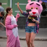 Фотография девушки в костюме розовой пантеры на улице. Девушка в розовом костюме и с головой в виде розовой пантеры, позирует на фоне городской среды.