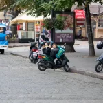 Фотография уличной сцены с мотоциклом и яркой рекламой на фоне. На заднем плане видны здания и другие элементы городской среды.