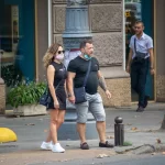 Фото тату на руке мужчины, стоящего рядом с девушкой в маске. Видны детализированные рисунки на плече и предплечье, выполненные в темных тонах.