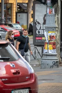 Фото тату на руке мужчины, идущего по улице. Видны детализированные рисунки на плече и предплечье, выполненные в темных тонах.