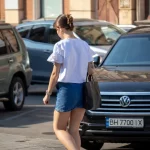Фото тату: девушка с татуировкой птицы на плече идет по улице. Рисунок выполнен в черных тонах, реалистичный стиль. Вид сзади.