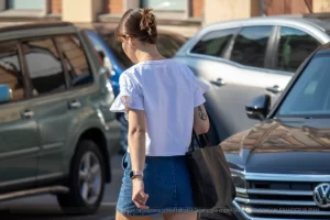 Фото тату: девушка с татуировкой птицы на плече идет по улице. Рисунок выполнен в черных тонах, реалистичный стиль. Вид сбоку.