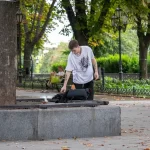 Фото татуировок на руках мужчины, сидящего на скамейке. Изображены абстрактные узоры и рисунок птицы.