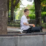 Фото татуировок на руках мужчины, сидящего на скамейке. Изображены абстрактные узоры и рисунок птицы.