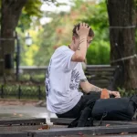 Фото татуировок на руках мужчины, сидящего на скамейке. Изображены абстрактные узоры и рисунок птицы.