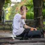 Фото татуировок на руках мужчины, сидящего на скамейке. Изображены абстрактные узоры и рисунок птицы.