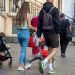 Фото тату на икре мужчины, идущего по улице с коляской. Татуировка выполнена в черных тонах, изображает абстрактный рисунок.