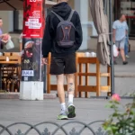 Фотография мужчины с татуировкой на икре, идущего по улице с рюкзаком. Татуировка изображает голову дракона в японском стиле. Уличная фотография.