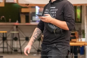 Крупный план татуировки на руке мужчины. Рисунок выполнен в черно-серых тонах и представляет собой сложный орнамент. Снимок сделан в стиле стрит-фотографии.