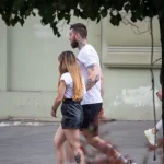 Фотография пары, идущей по улице. У мужчины видна татуировка на руке, а у девушки - на ноге. Снимок в стиле стрит-фотографии, подчеркивающий индивидуальность и стиль.