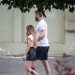 Фотография пары, идущей по улице. У мужчины видна татуировка на руке, а у девушки - на ноге. Снимок в стиле стрит-фотографии, подчеркивающий современный стиль.