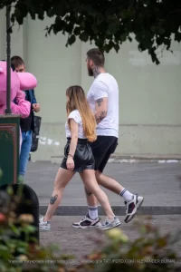 Фотография пары, идущей по улице. У девушки видна татуировка на ноге, а у мужчины - на руке. Снимок в стиле стрит-фотографии, подчеркивающий индивидуальность.