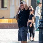 Фото тату на руке мужчины, говорящего по телефону на улице. Татуировка выполнена в черном цвете и покрывает большую часть предплечья.