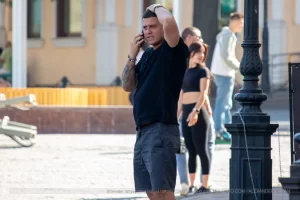 Фото тату на руке мужчины, говорящего по телефону на улице. Татуировка выполнена в черном цвете и покрывает большую часть предплечья.