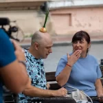 Фото тату: Мужчина с татуировкой на плече и луковицей на голове, сидящий на скамейке с женщиной. Уличная фотография, демонстрирующая необычный образ и татуировку.